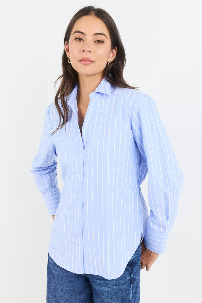 Woman wearing a light blue striped shirt and jeans against a white background