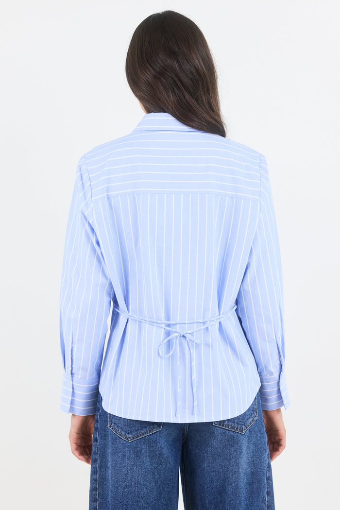Woman wearing a light blue striped shirt with a tie waist on a white background