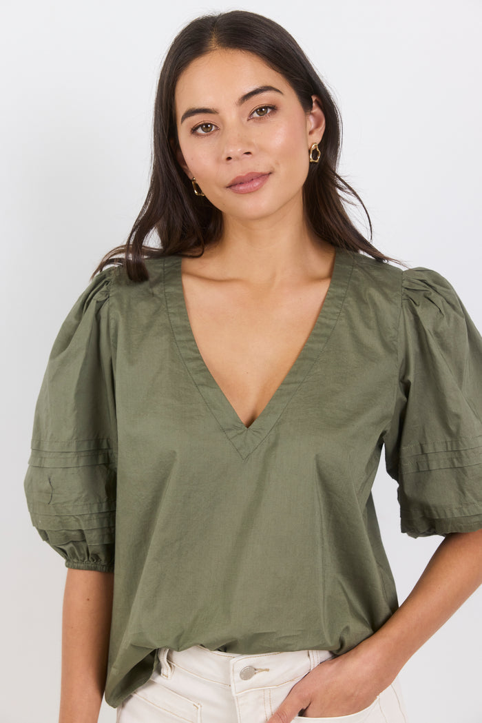 Woman wearing a green blouse with puffed sleeves against a white background