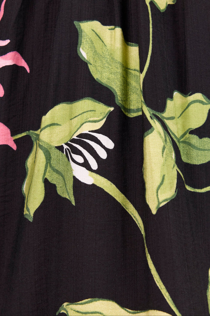 Close-up of a black fabric with a botanical print featuring green leaves, pink flower petals, and white flower centers.