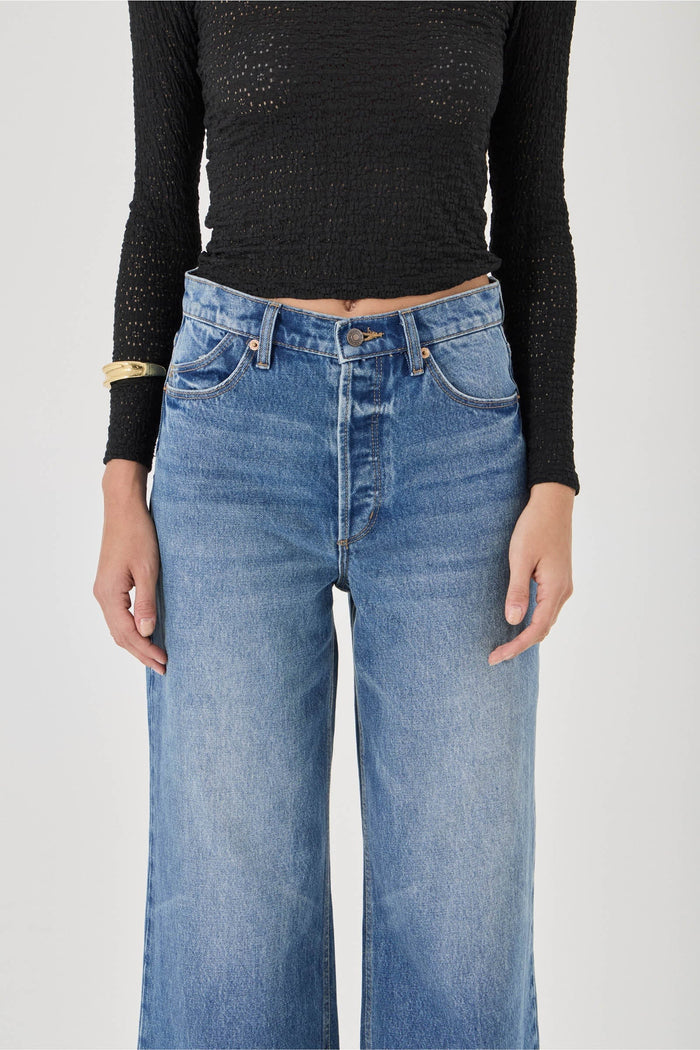 Person wearing blue jeans and a black long-sleeve top on a plain background