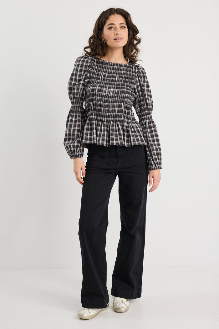 Woman wearing a patterned top and black pants on a white background