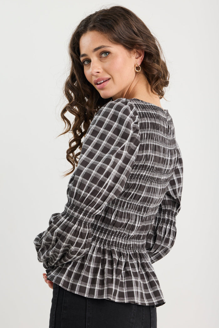 Woman wearing a black and white checkered blouse with ruffled details on a white background