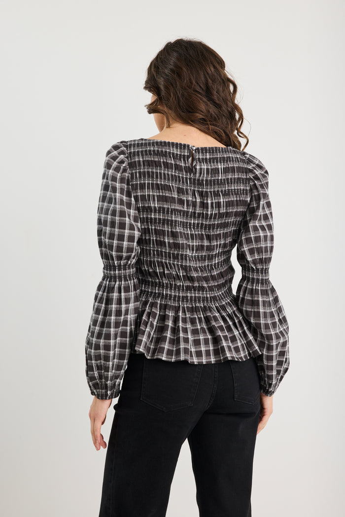 Woman wearing a black and white checkered blouse with long sleeves on a plain background