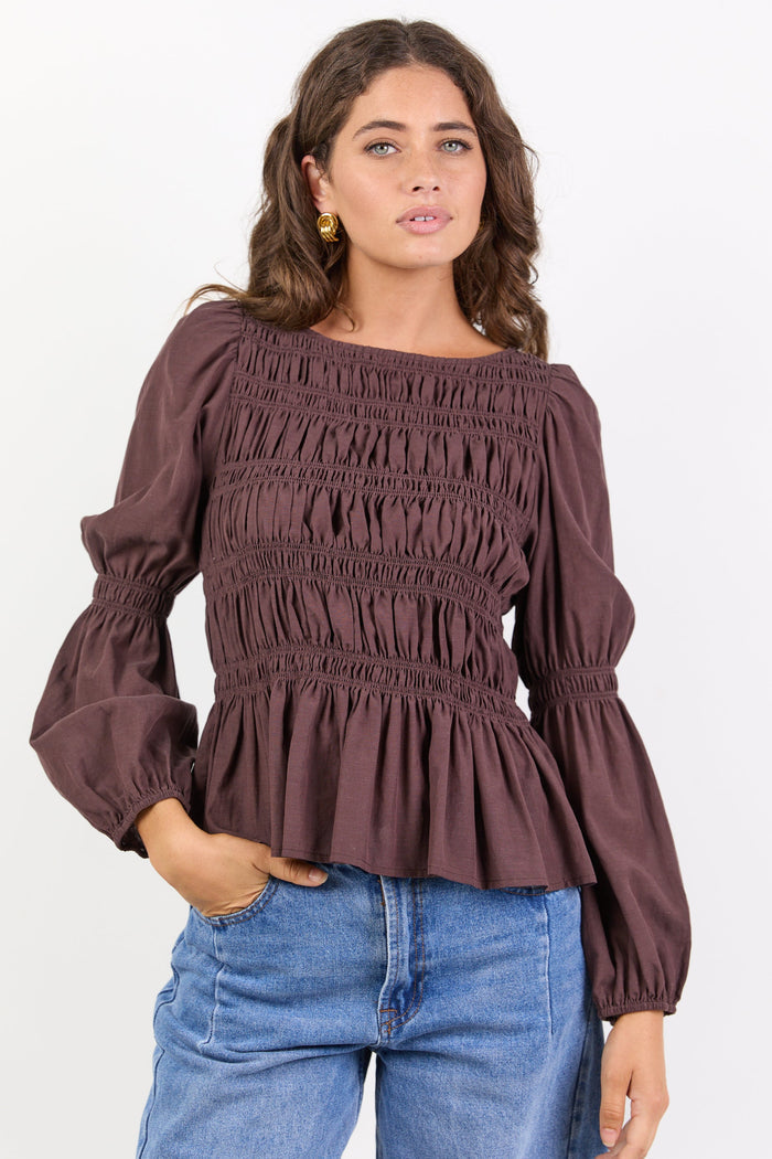Woman wearing a brown smocked blouse and blue jeans on a white background