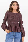 Woman wearing a brown smocked blouse and blue jeans on a white background