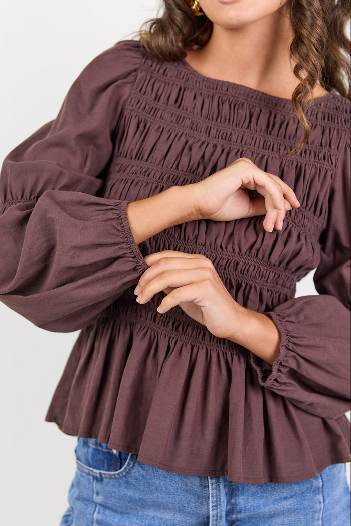 Brown smocked blouse with long sleeves worn by a person on a white background