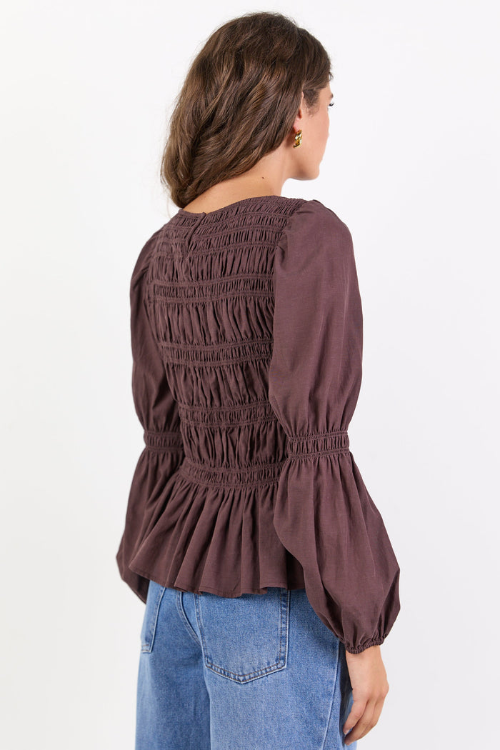 Woman wearing a brown smocked blouse and blue jeans on a white background