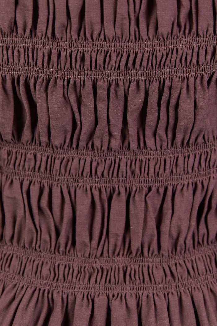 Close-up of a maroon dress with smocked waist and long sleeves.