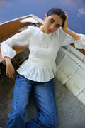 Woman wearing a white blouse and blue jeans sitting on a boat.
