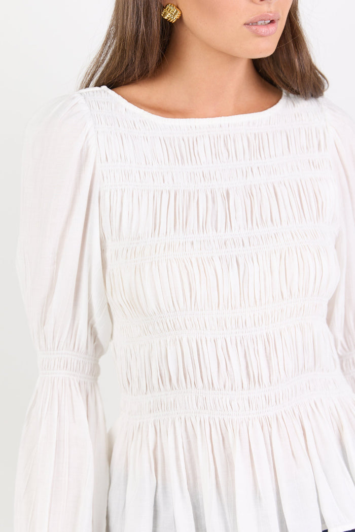 Woman wearing a white blouse with smocked details on a plain background