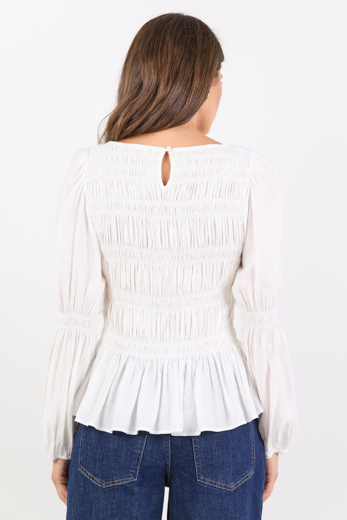 Woman wearing a white blouse with a pleated design and blue jeans on a white background