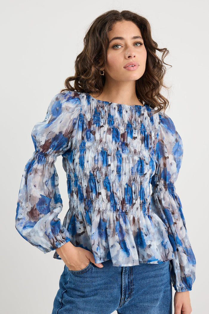 Woman wearing a blue patterned blouse and jeans against a white background