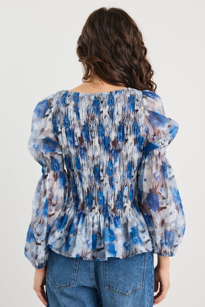 Woman wearing a blue and white patterned blouse with blue jeans on a plain background