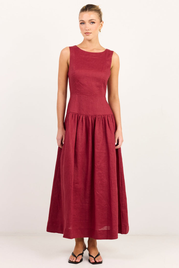 A woman modeling a sleeveless, high-neck, midi-length A-line dress in a deep burgundy or maroon shade, standing against a plain white studio background.