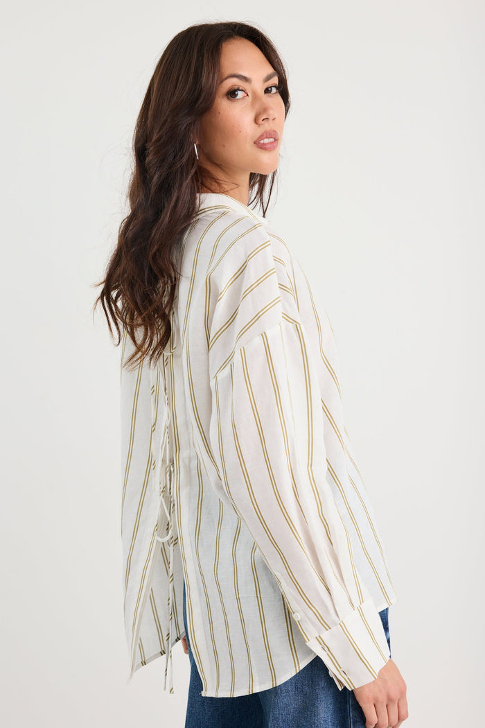 Woman wearing a white blouse with gold stripes against a plain background