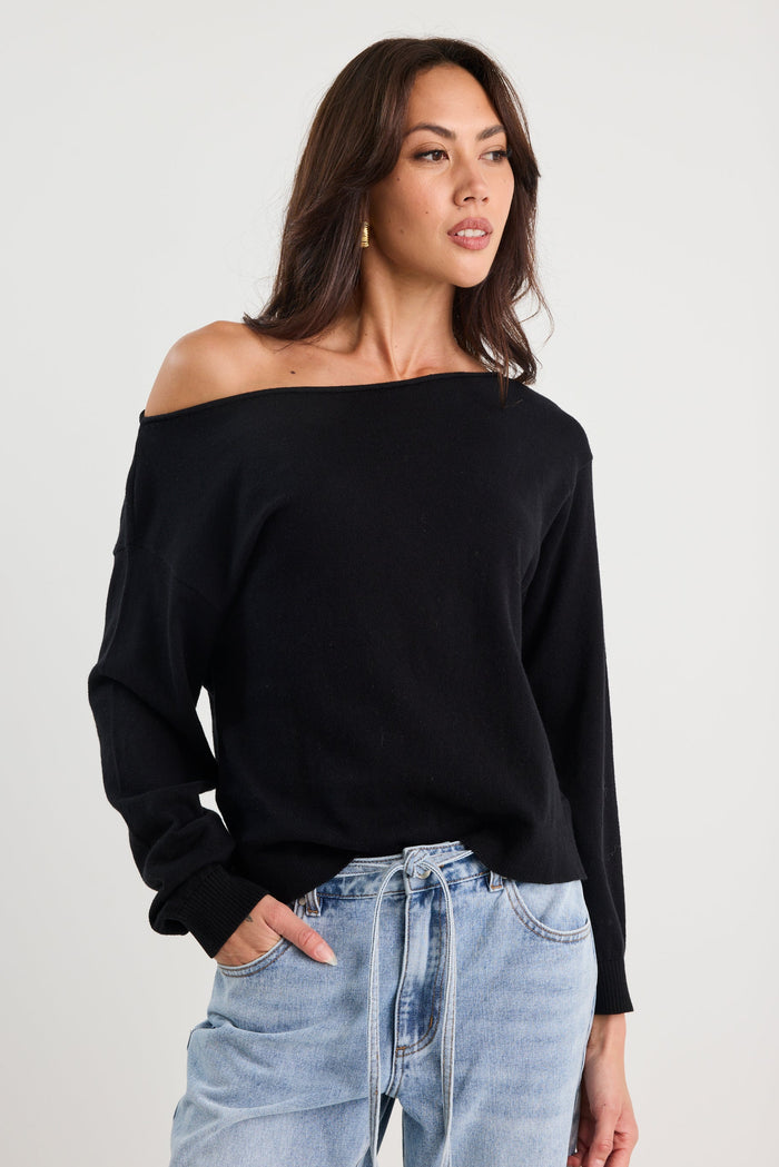 Woman wearing a black off-shoulder top and light blue jeans on a white background
