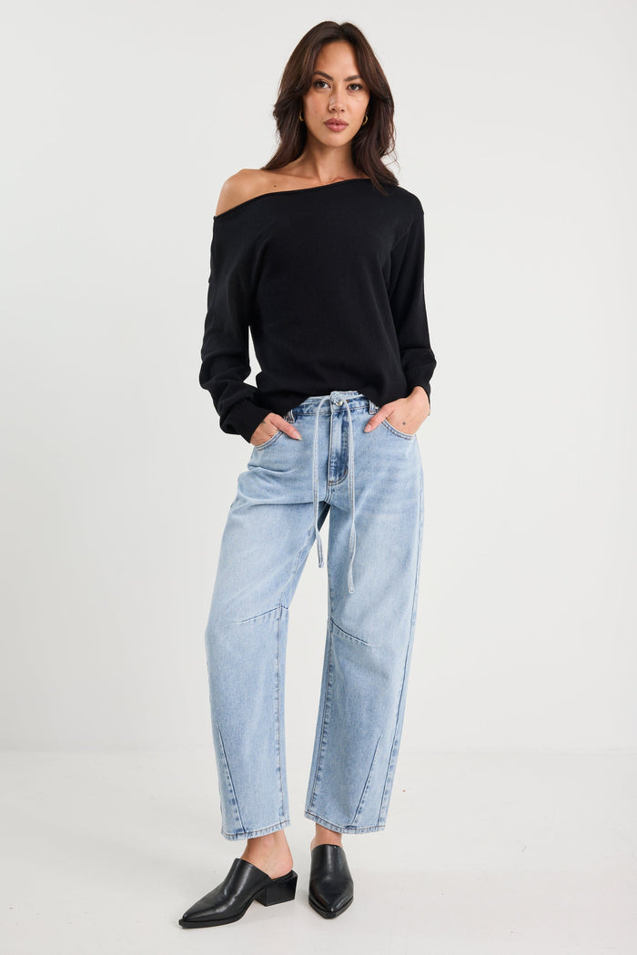 Woman wearing a black off-shoulder top and light blue jeans on a white background