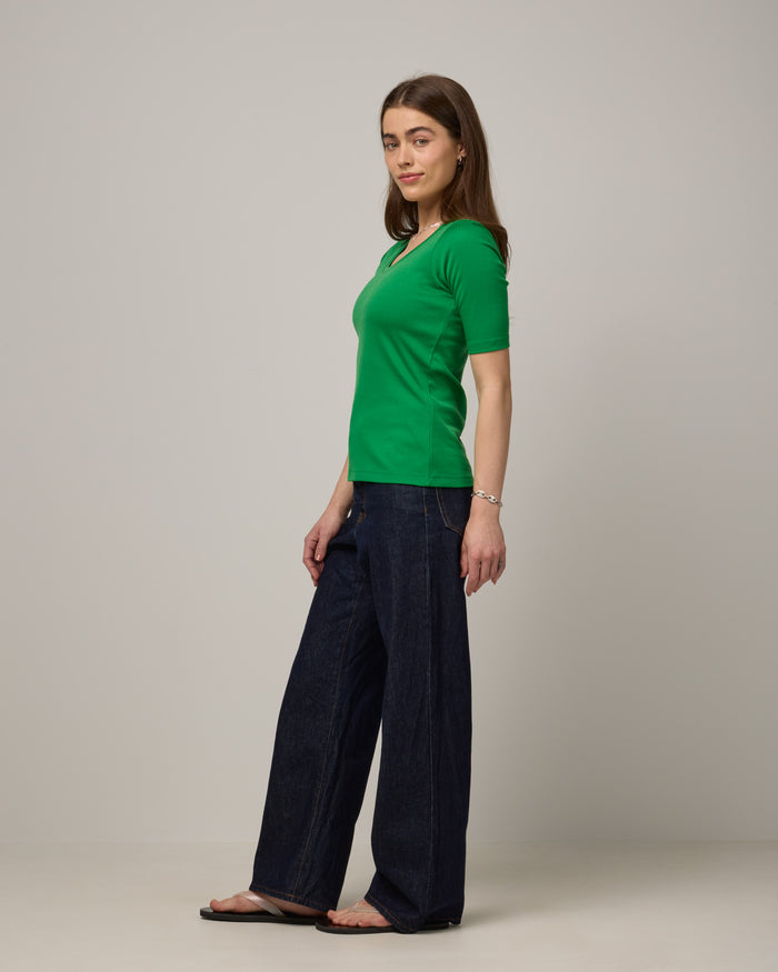 Model wearing Celine Ribbed Elbow Sleeve Tee in Verde, a bright Kelly green color. Celine Ribbed Elbow Sleeve Tee is a merino wool short sleeve, scoop neck tee available in sizes XS-3X.