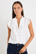 Woman wearing a sleeveless white blouse with ruffle detailing down the front and mixed buttons, paired with dark denim jeans.