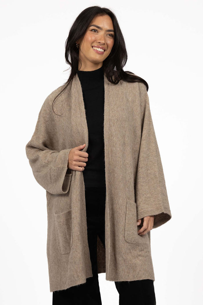 Woman wearing a beige coat over a black outfit on a white background