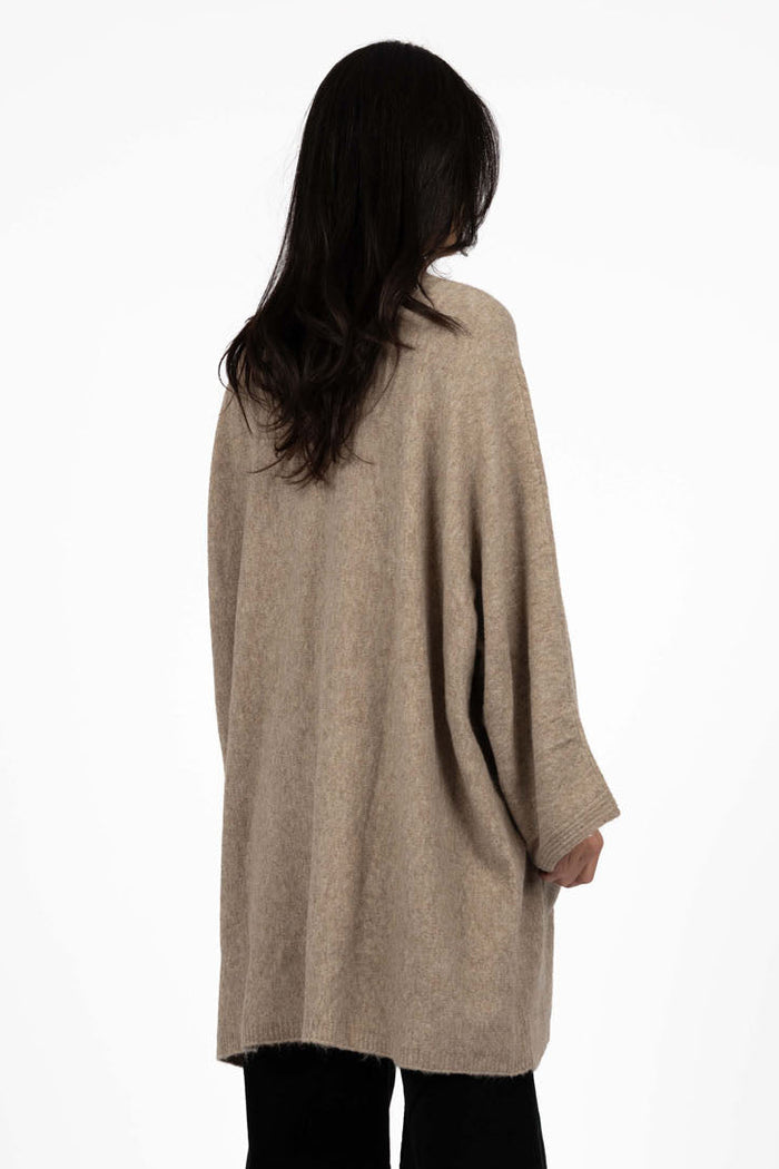 Person wearing a beige cardigan and black pants on a white background