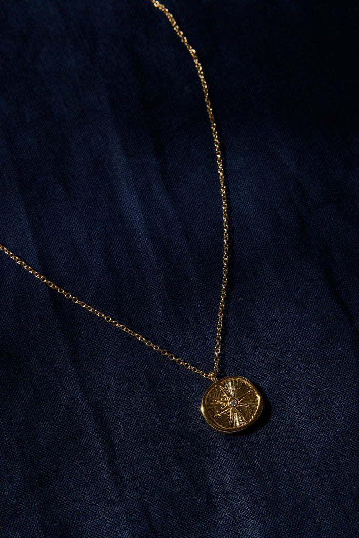 Gold necklace with a round pendant on a dark blue fabric background