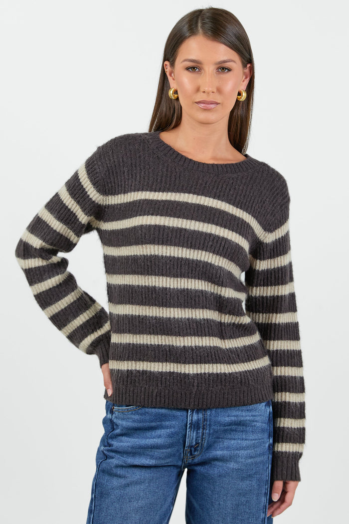 Woman wearing a black and beige striped sweater with blue jeans on a white background