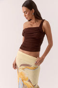 Woman wearing a brown one-shoulder top and a yellow skirt with a floral design on a white background