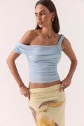 Woman wearing a light blue off-shoulder top and a beige skirt with a pattern.