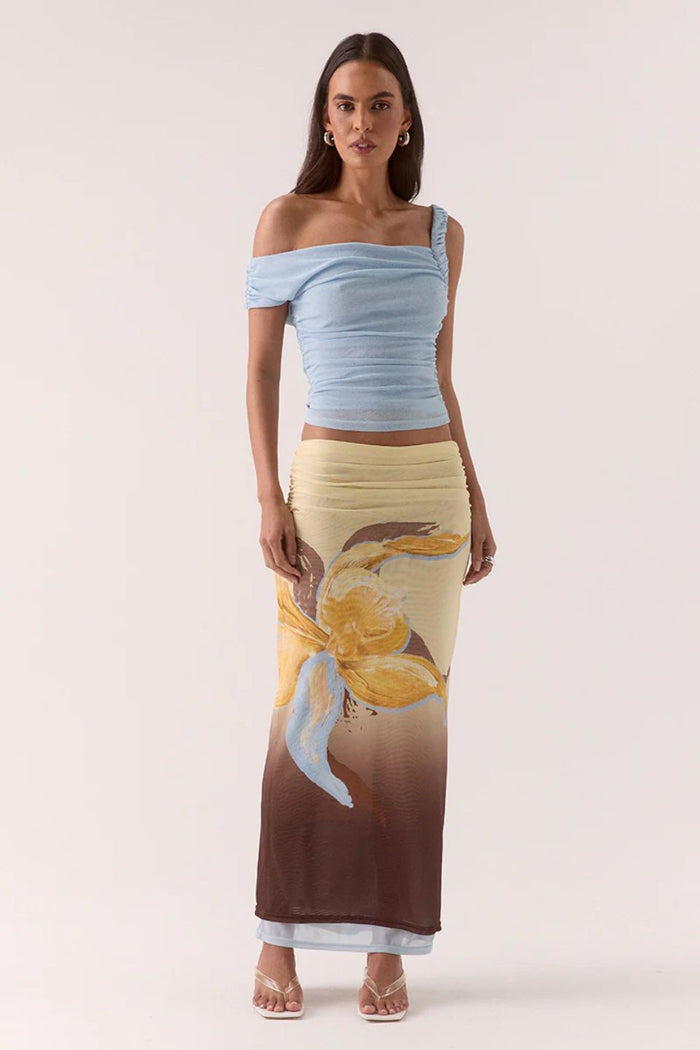 Woman wearing a light blue off-shoulder top and a long, patterned skirt on a white background