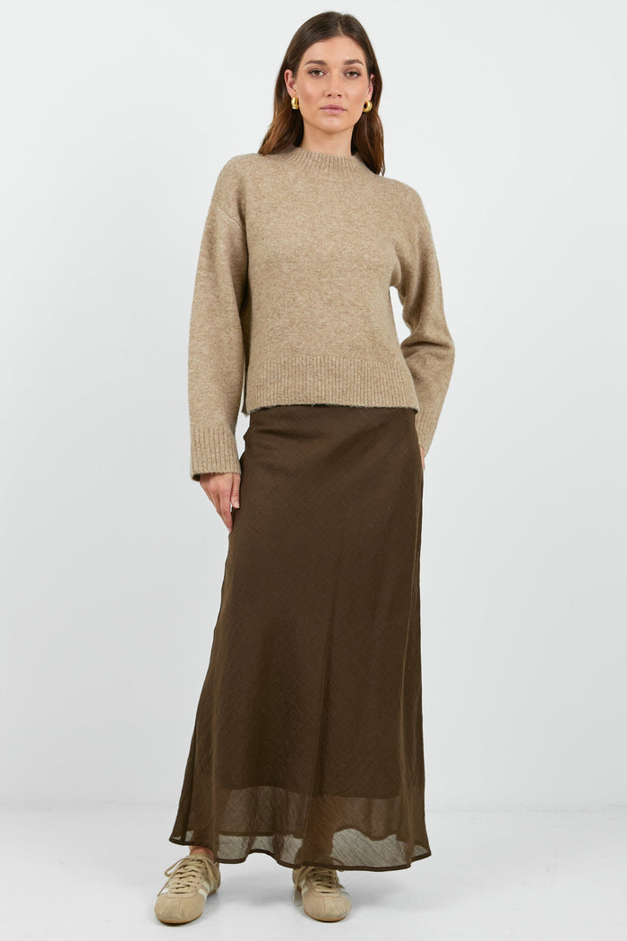Woman wearing a beige sweater and brown skirt on a white background