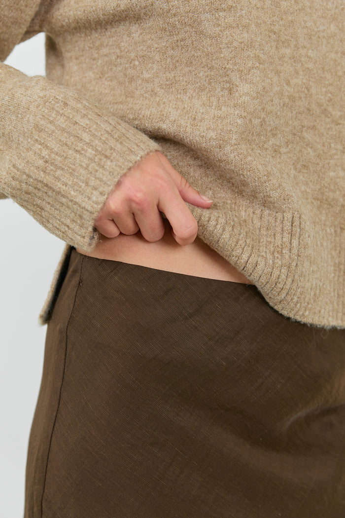 Close-up of a person wearing a beige sweater and brown pants on a white background