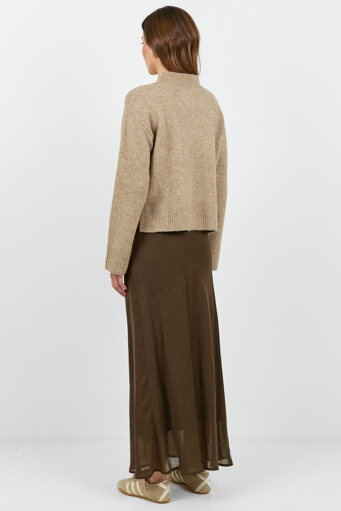 Person wearing a beige jacket and brown skirt on a white background
