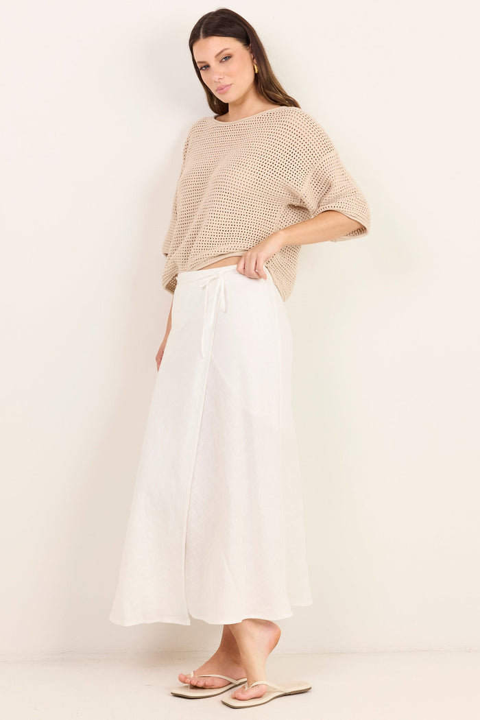 A woman modeling a beige knit short-sleeve top and white wide-leg skirt against a plain off-white studio background.