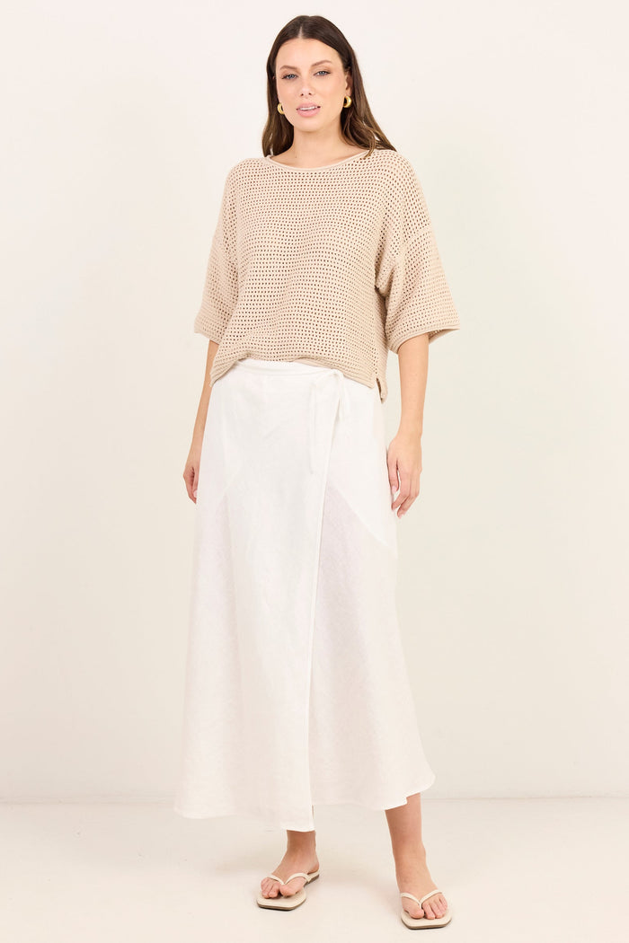 A woman modeling a beige knit short-sleeve top and white wide-leg midi skirt against a plain off-white studio background.