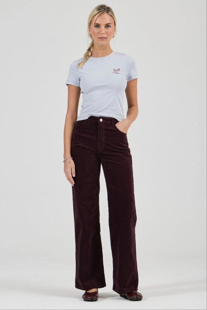 Woman wearing a light gray t-shirt and dark brown corduroy pants on a white background