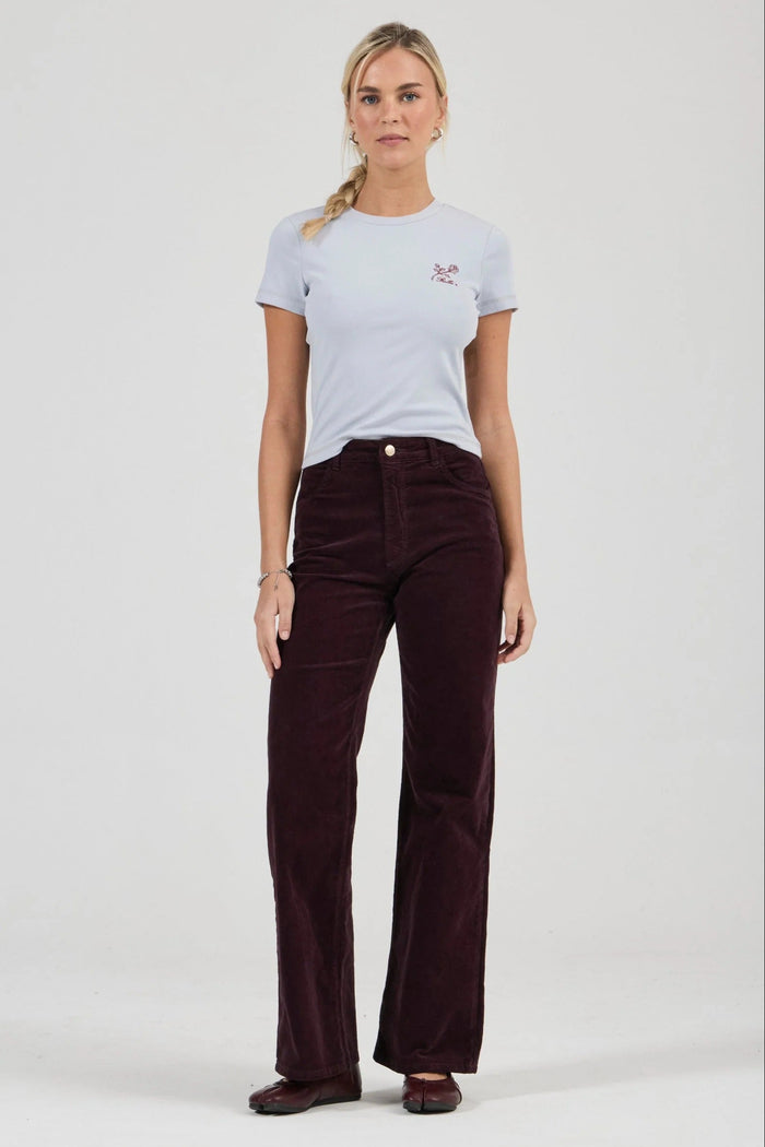 Woman wearing a light blue t-shirt and dark brown corduroy pants on a white background