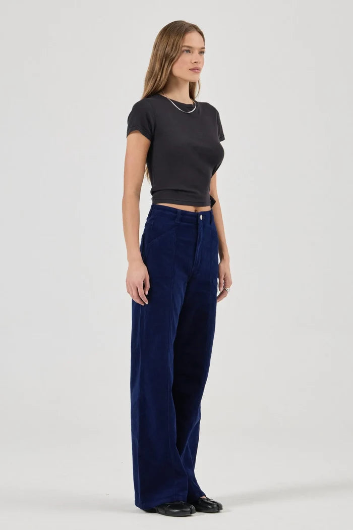 Woman wearing a black crop top and blue velvet pants on a white background