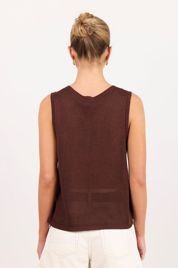 A woman viewed from the back wearing a sleeveless dark brown knit top and white shorts against a plain white background.