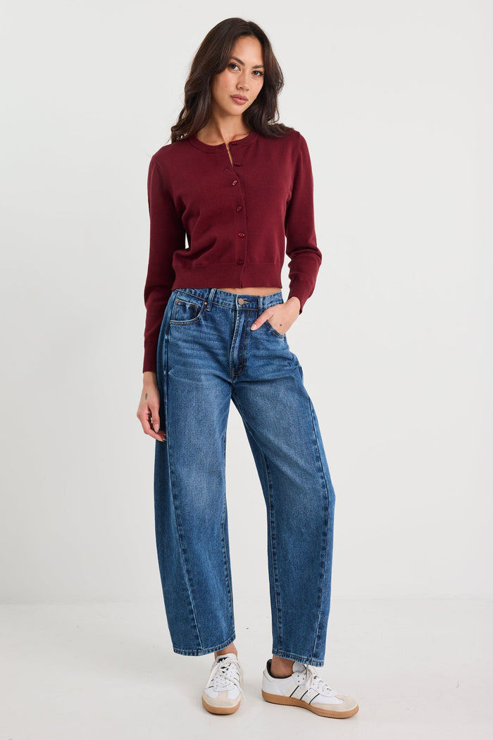 Woman wearing a burgundy sweater and blue jeans on a white background