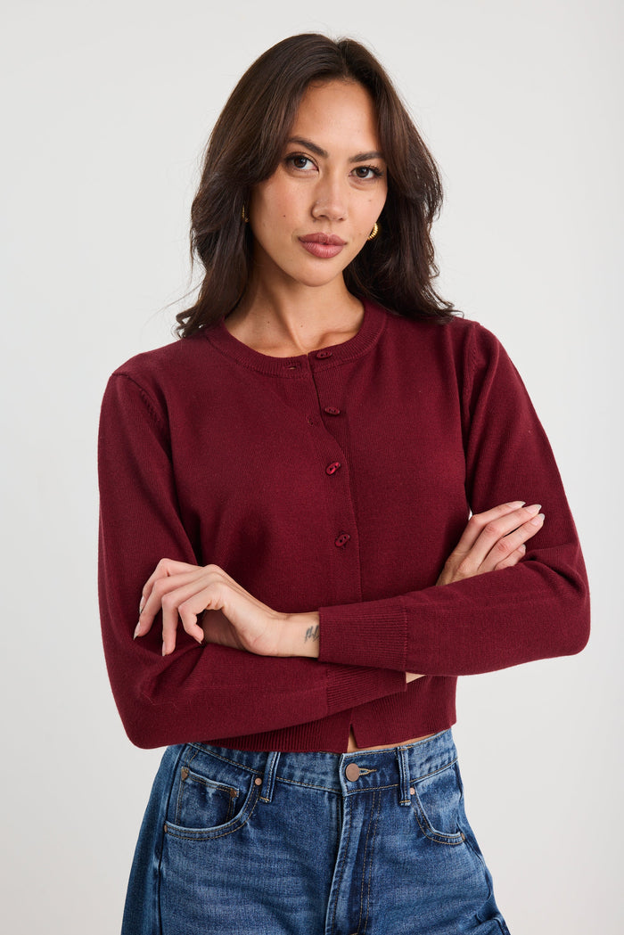 Woman wearing a burgundy sweater and blue jeans against a white background