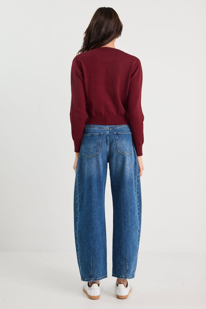 Person wearing a burgundy sweater and blue jeans on a white background