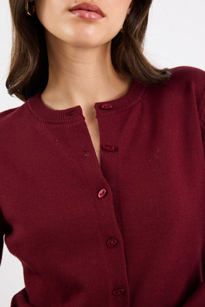Close-up of a person wearing a burgundy cardigan with a plain background