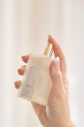 Hand holding a white bottle with a gold cap against a light background