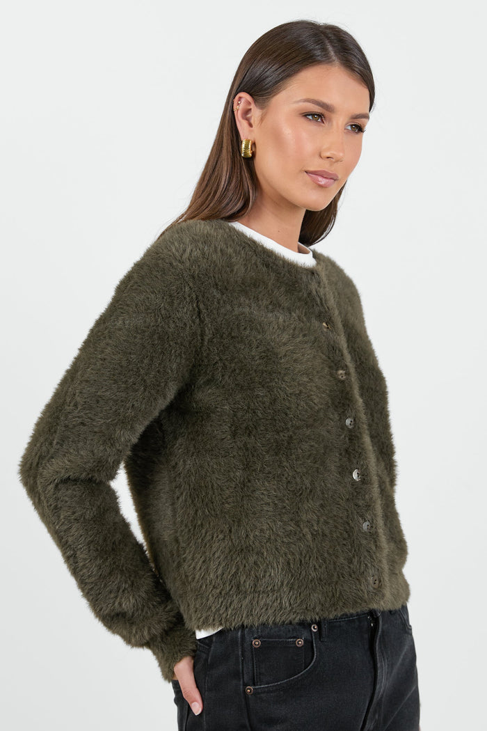 A woman wearing a soft, khaki fluffy cardigan with a round neckline and button-down front, paired with high-waisted black jeans.
