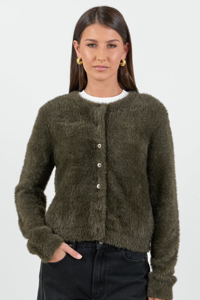 A woman wearing a soft, khaki fluffy cardigan with a round neckline and button-down front, paired with high-waisted black jeans.