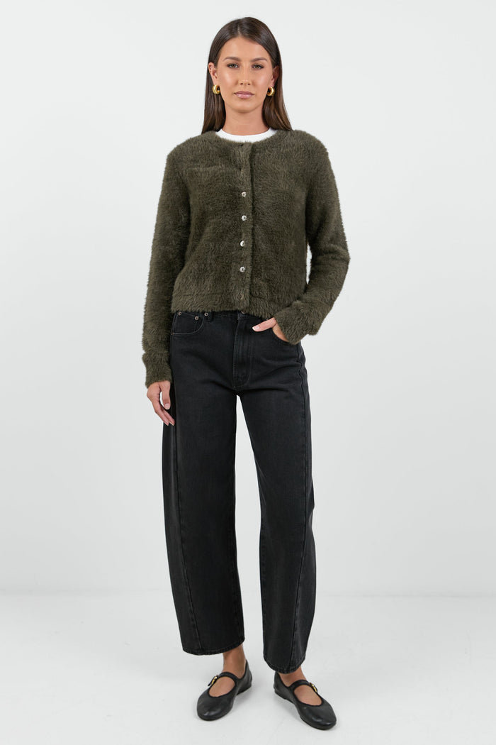 A woman wearing a soft, khaki fluffy cardigan with a round neckline and button-down front, paired with high-waisted black jeans.