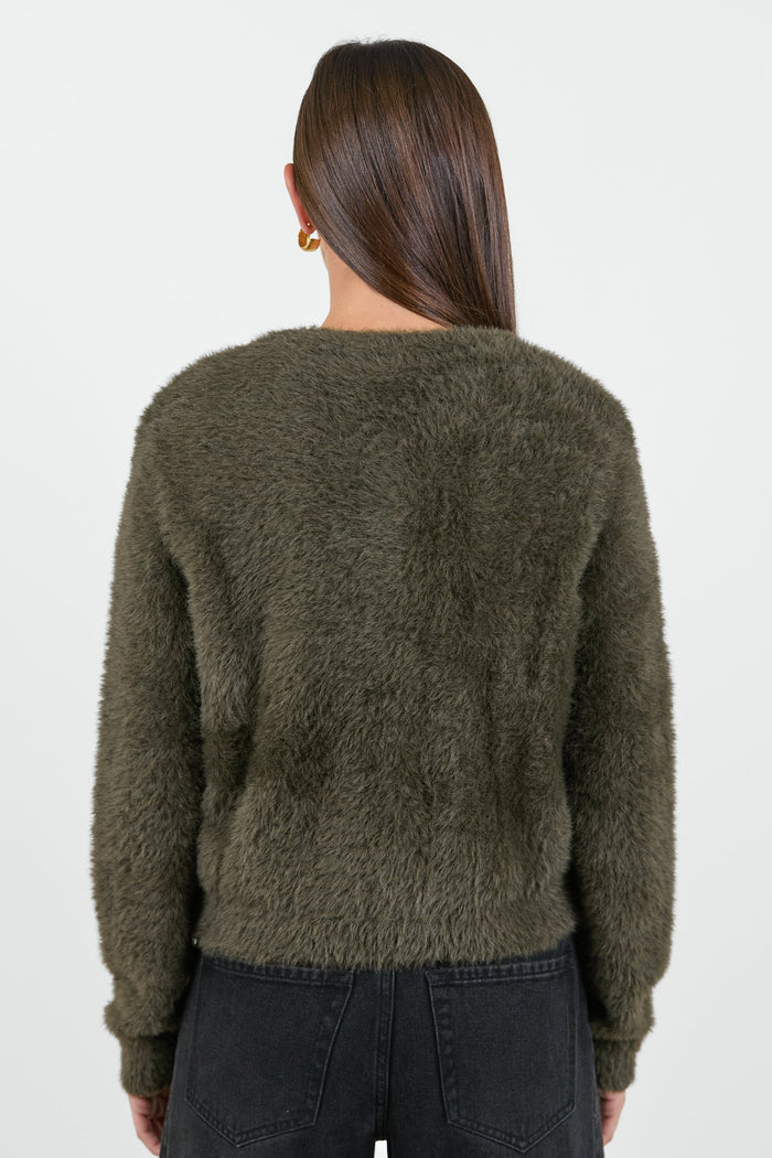 A woman wearing a soft, khaki fluffy cardigan with a round neckline and button-down front, paired with high-waisted black jeans.