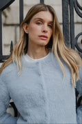 Woman wearing a light blue fuzzy sweater in front of an iron gate.